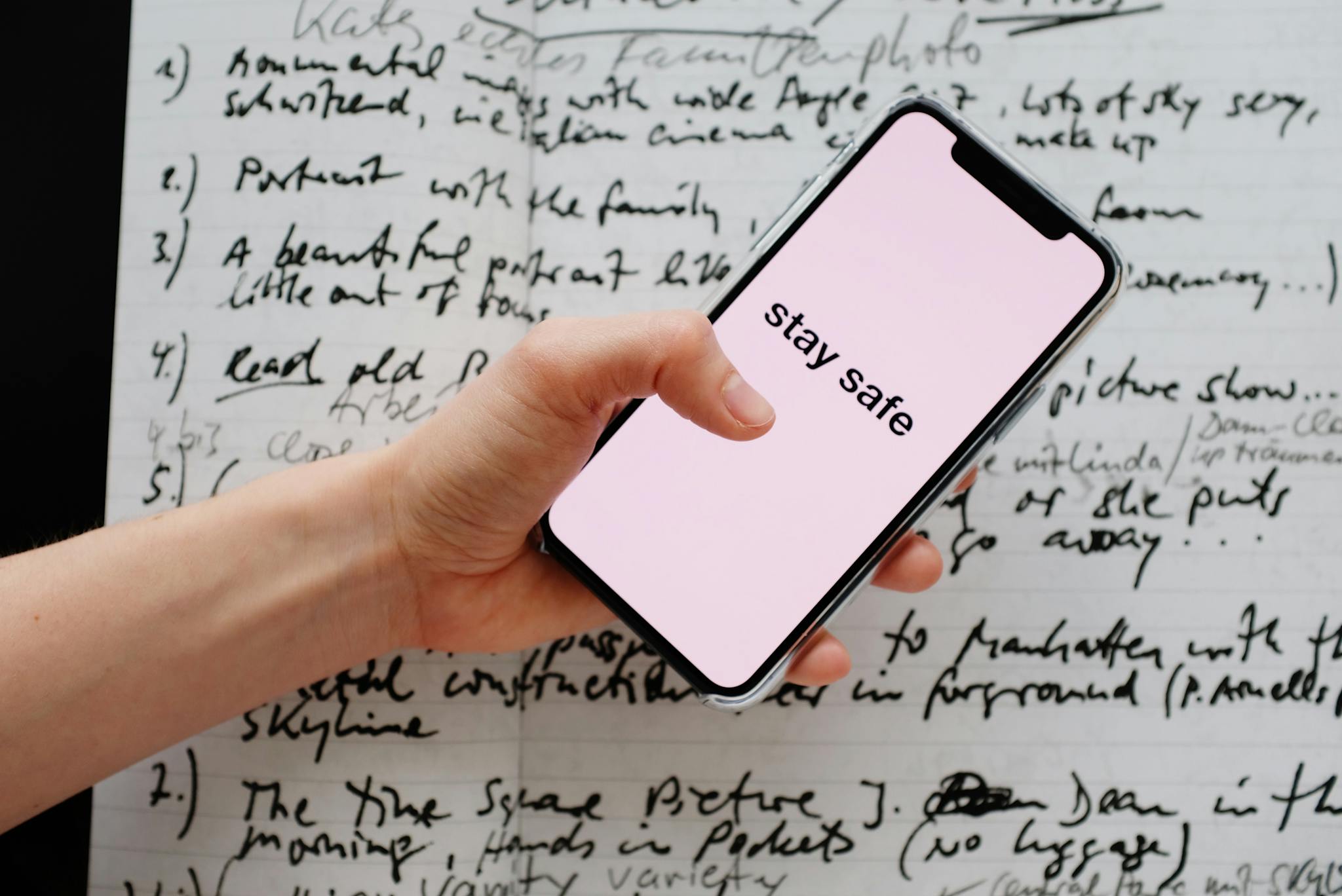 Hand holding a smartphone displaying 'Stay Safe' over a handwritten notes background.